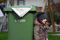 Kleines Mädchen neben einer grünen Papiertonne