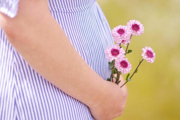 Schwangere Frau hält Blumen vor ihren Babybauch