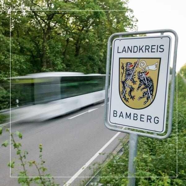 Im Vordergrund sieht man ein Schild mit dem Wappen des Landkreises Bamberg. Im Hintergrund fährt ein Bus.