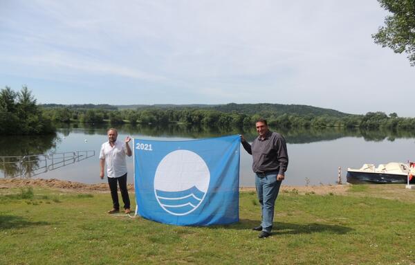 Detlef Sperlich und Bürgermeister Jochen Weber (Gemeinde Michelau i.OFr.) mit der Blauen Flagge am Rudufersee bei Schwürbitz. Das Geländer im Hintergrund hilft Menschen, die nicht so gut zu Fuß sind, sicherer ins Wasser zu kommen.